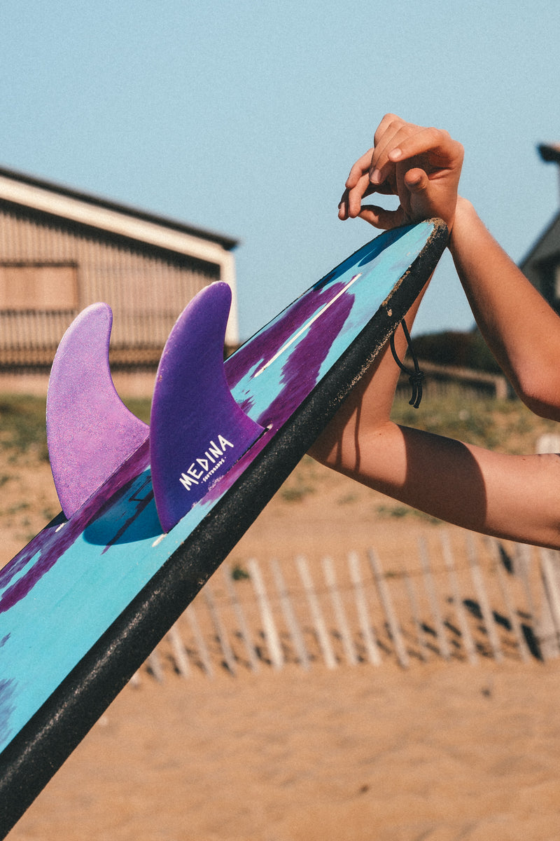 Set of surfboard fins laid on a board at the edge of the beach