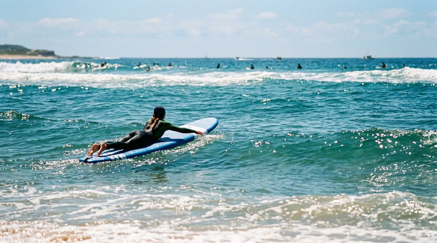 Surfer seen from behind lying on a foam surfboard, paddling before the pop-up