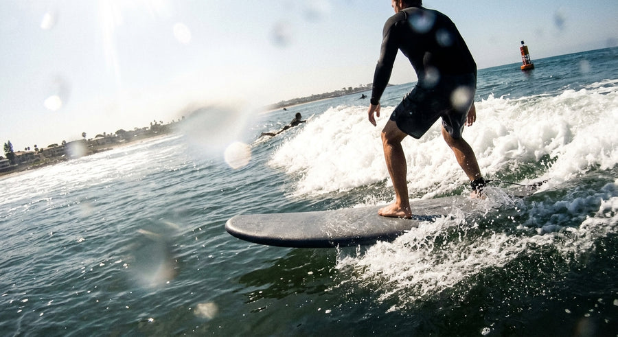 Surfer seen from behind standing with bent knees on a foam surfboard