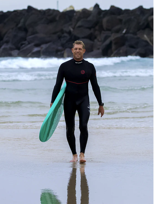Surfeur debout sur la plage tenant une planche de surf en mousse
