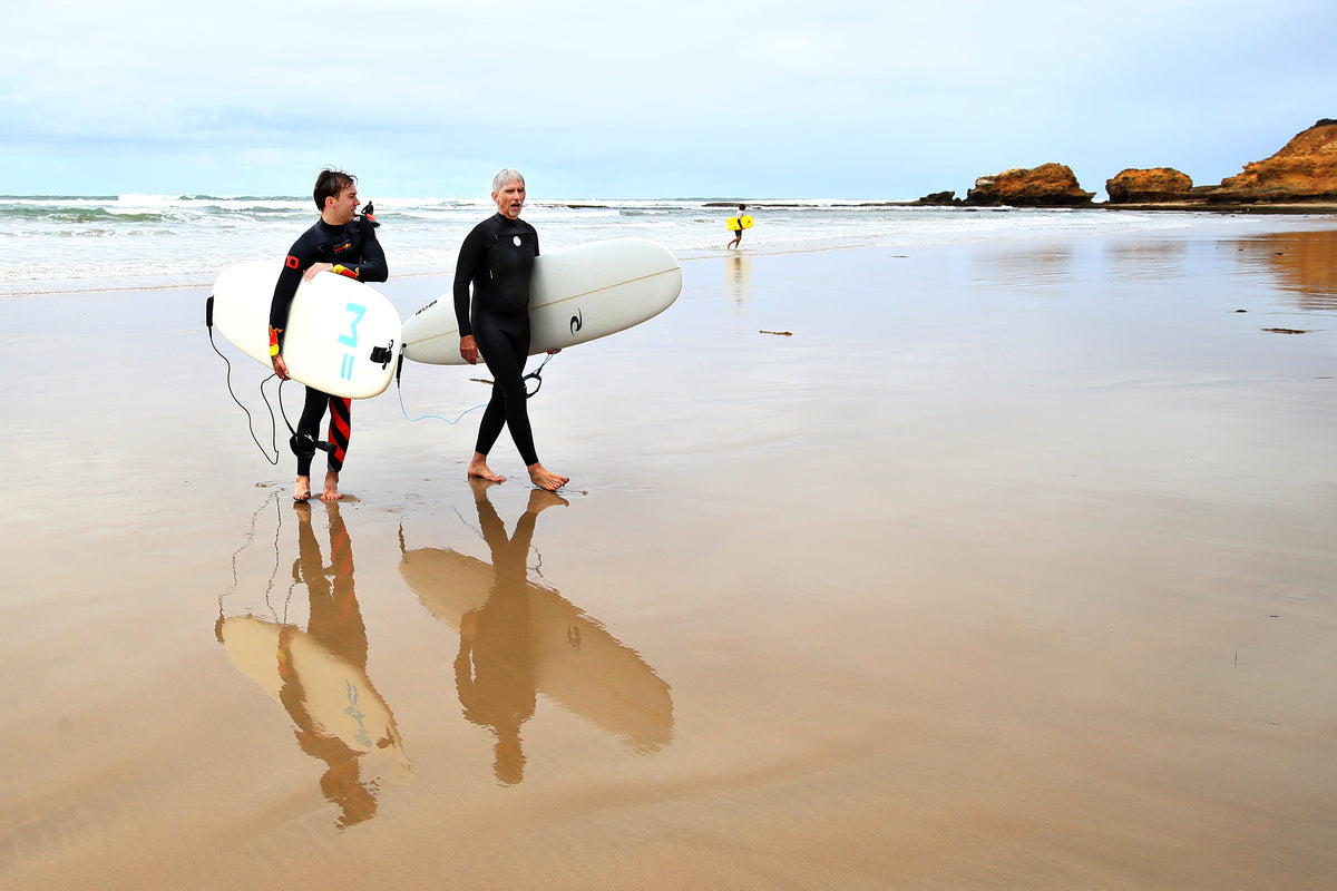 Beginner seen from behind walking towards the waves with a foam surfboard