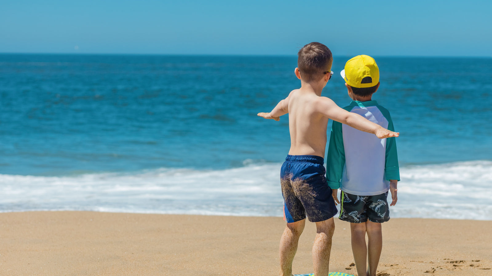 Child seen from behind on the beach with a foam surfboard